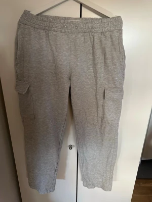 Grå cargo mjukisbyxor med fickor - Säljer ett par grå mjukisbyxor med cargofickor på sidorna och bakficka. Byxorna har resår i midjan och är gjorda i mjukt sweatshirtmaterial. Perfekta för chill dagar eller när du vill ha det bekvämt. Storlek L men skulle säga att den passar M också.