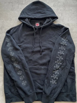 Independent x Thrasher Pentagram Cross Hoodie - L - Svart hoodie från Independent med tryckta loggor längs båda ärmarna. Klassisk känguruficka framtill och justerbar dragsko i huvan. Tillverkad i mjuk bomullsblandning, perfekt för en avslappnad streetwear-look.