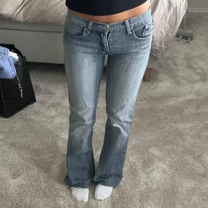 Ljusblåa Victoria Beckham bootcut jeans - Säljer ett par ljusblåa bootcut jeans från Victoria Beckham med broderade kronor på bakfickorna. Jeansen har låg midja, klassisk femficksdesign och är tillverkade i jeansmaterial. Perfekta för dig som gillar en avslappnad och trendig look.