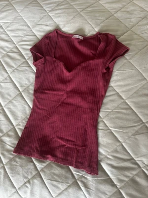 Ribbad vinröd topp från Gina Tricot - Snygg, vinröd topp i ribbat och stretchigt material. Smickrande sweetheart-ringning och figurnära passform. Mycket fint skick! 