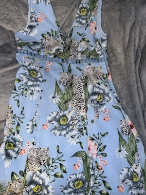 Blommig blå kortklänning med leoparder - Snygg ljusblå kortklänning med djup v-ringning och brett axelband.