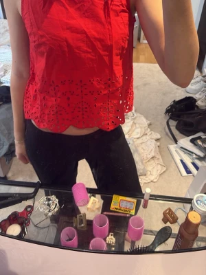 Röd broderad croppad linnetopp - Snygg röd croppad linnetopp med broderade detaljer och hålmönster längst ner. Toppen är ärmlös och har en luftig passform, perfekt för varma dagar. Utan prislapp, men aldrig använt!