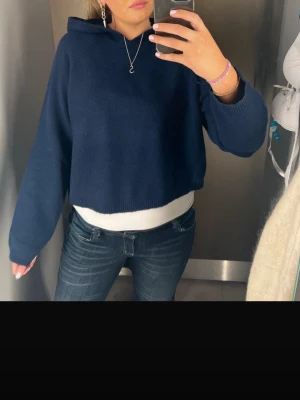 Mörkblå stickad  hoodie - Säljer en mörkblå stickad hoodie med huva och långa ärmar. Hoodien har en enkel och stilren design utan tryck eller logga, och är gjord i ett mjukt stickat material som känns skönt mot huden. Perfekt för en avslappnad och trendig look. Jättefin endast testad! 