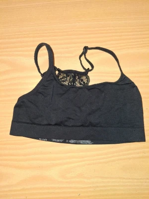 Svart spetsdetaljerad bralette - Svart bralette med smala axelband och snygga spetsdetaljer i ryggen. Mjuk och stretchig modell som passar perfekt under toppar och tröjor. Enkel och stilren design med en feminin touch tack vare spetsen.
