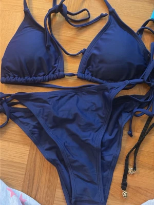 Mörkblå bikini med knyt - Snygg mörkblå bikini med klassisk trekantsmodell på överdelen och knyt både i rygg och nacke. Underdelen har matchande knyt i sidorna. 