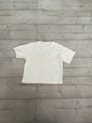 Vit basic t-shirt från Lindex - En enkel vit t-shirt från Lindex i mjuk bomull. Klassisk rund halsringning och korta ärmar, perfekt till alla outfits. Passar dig som gillar en clean och stilren look.