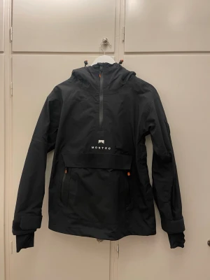 Skidjacka Montec, storlek S - Svart vindjacka från Montec med huva och halv dragkedja framtill. Anorakmodell. Utan defekter, använd endast ett fåtal gånger.