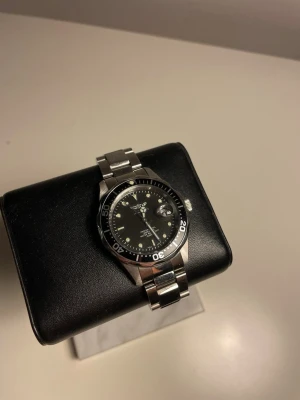Invicta klocka - Stilren klocka från Invicta med svart urtavla och datumvisning. Boetten och länken är i blankt rostfritt stål och har en klassisk rund form. Urtavlan har tydliga markeringar och vridbar bezel i svart. Vattentät upp till 200m