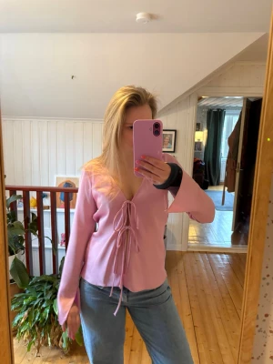 Rosa topp med snörning Zara  - Säljer en ljusrosa omlottopp med långa ärmar och snygg snörning framtill. Toppen har v-ringning och vida ärmslut för en trendig look. Perfekt att styla med jeans eller kjol för en cool outfit.