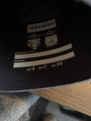 Svarta Hunter gummistövlar EU 38 - Klassiska svarta gummistövlar från Hunter i storlek EU 38. Stövlarna har robust sula med röd detalj och Hunter-logga både på insidan och baksidan. Perfekta för regniga dagar och festivaler. Tillverkade i slitstarkt gummi med bekväm passform.