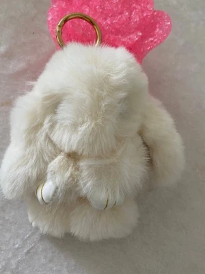 Vit fluffig kanin nyckelring - Supersöt och fluffig kaninformad nyckelring i vit fuskpäls med guldfärgad ring. Perfekt att hänga på väskan eller använda till nycklar. Tassarna har vita detaljer med guldfärgade linjer. Ger en gullig touch till din stil.