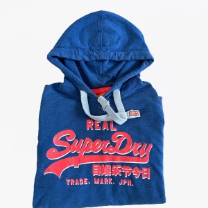 Blå Superdry Hoodie  - Säljer en riktigt snygg superdryhoodie i storlek L. Den är i använt skick men har fortfarande mycket kvar att ge. Inga större defekter på den heller!   Pris 399 Skick 8,5/10 Storlek L   Hör av er vid frågor eller prisförslag! Skambud undanbedes😃