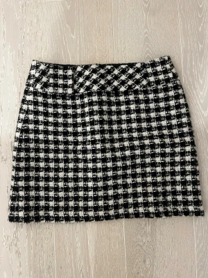 Rutig svartvit kjol från CCDK - Snygg kort kjol från CCDK i svartvitt rutigt mönster. Kjolen har en klassisk rak passform och bälteshällor i midjan. Perfekt att matcha med en enkel topp eller stickad tröja för en trendig look. Rök- och djurfritt hem.