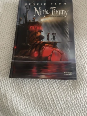Ninja Timmy och resan till Sansoria - En spännande bok av Henrik Tamm med hård pärm och fantasifullt omslag i mörka färger. Boken handlar om Ninja Timmy och hans gäng på äventyr. Perfekt för dig som gillar äventyr, katter och snygga illustrationer.