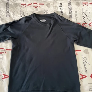 Marinblå/svart tröja från Mads Nørgaard - Snygg svart tröja från Mads Nørgaard med långa ärmar och stilrena ränder längs ärmarna. Perfekt för en avslappnad och trendig look. Passar bra till både jeans och chinos. Men som man kan se på bilderna är tröjan lite solblek också. 