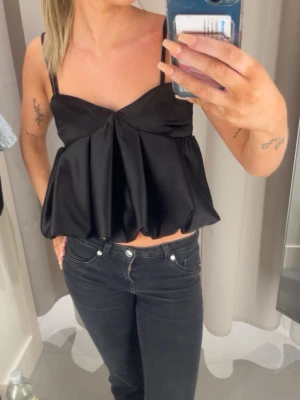 Svart satinlinnetopp med tunna band - Trendig svart linnetopp i satin med tunna axelband och volang känsla 