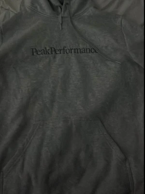 Grå hoodie från Peak Performance - Snygg grå hoodie från Peak Performance med klassisk logga broderad på bröstet. Hoodien har huva med dragsko och en stor magficka framtill. Tillverkad i mjukt bomullsmaterial som är skönt att bära. 💕💕
