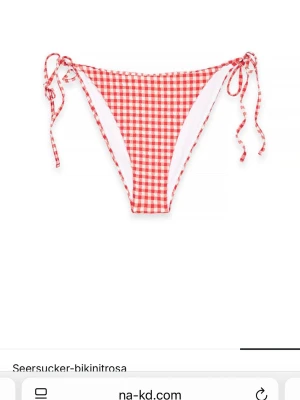 Rödvit seersucker bikinitrosa NA-KD - Snygg bikinitrosa från NA-KD i seersucker-material med rödvitt rutigt mönster. Modellen har knytband i sidorna för justerbar passform och en klassisk, lite högre skärning. Perfekt för strandhäng och poolparty.