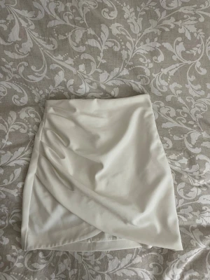 Vit kjol Zara - Säljer en stilren vit kjol från Zara i kort modell. Kjolen har en snygg omlottdetalj framtill och är tillverkad i ett mjukt tyg som känns bekvämt. 