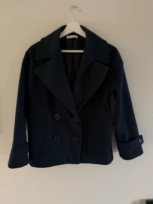 Mörkblå kappa  - Stilren mörkblå kappa från Designbysi med bred krage och dubbelknäppning framtill. Använt ett fåtal gånger och skulle säga att den passar xs-m.