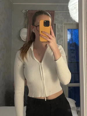 Vit ribbad ziptröja från Stradivarius  - Trendig vit ribbad ziptröja från Gina Tricot med lång ärm och krage. Tröjan är croppad och har dragkedja framtill som kan öppnas både uppifrån och nerifrån. Perfekt till jeans eller kjol för en clean look.