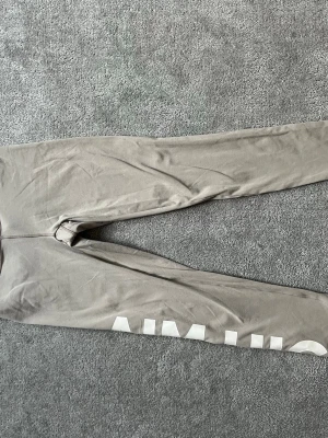 Beige leggings med tryck AIM HIGH - Säljer ett par beige leggings med vit text 'AIM HIGH' längs ena benet. De har en tight passform och är perfekta för träning eller chill. Materialet känns mjukt och stretchigt, vilket gör dem riktigt bekväma att ha på sig. Storlek Xs från amin.