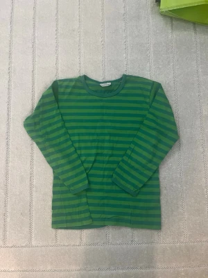 Grön randig långärmad topp Marimekko  - Snygg långärmad topp från Marimekko i gröna nyanser med horisontella ränder. Klassisk rund halsringning och mjukt bomullsmaterial som känns skönt mot huden. Perfekt för dig som gillar färg och mönster. Är ungefär som en xxxs/xxs