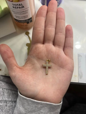 Guldfärgat korshalsband - Snyggt halsband med ett guldfärgat kors som hänge. Korset har en strukturerad yta som ger extra detalj och glans. Perfekt för dig som gillar stilrena och klassiska smycken. Passar till många olika looks och är lätt att matcha med andra accessoarer.