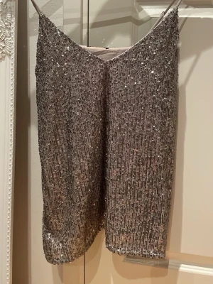 Glittrig silverfärgad linnetopp från Amisu (läs nedan för storleksbeskrivning) - Supersnygg glittrig linnetopp i silver med tunna axelband och v-ringad hals. Perfekt för att sticka ut med sitt paljettmönster och skimrande material. Ger en lyxig känsla och passar till många olika stilar. (Tyvärr är lappen för storleken borta, men kan skicka mått om de önskas, jag skulle uppskatta att den är i storlek S/M då den är väldigt stretchig och har justerbara band)!!! Använt en gång. 