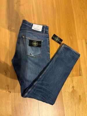 Blå jeans från Stone Island - Snygga blå jeans från Stone Island med klassisk femficksmodell och ikonisk logotyp på bakfickan. Jeansen är tillverkade i denim med lätt tvättad look. Perfekta för dig som gillar streetwear och vill sticka ut. Tillkommer även än extra Stone Island badge som man ser på bilderna