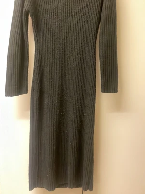 Svart ribbad stickad klänning Gina Tricot - Svart långärmad stickad klänning från Gina Tricot i ribbat material. Klänningen har en kroppsnära passform och är i en längre modell, perfekt för dig som gillar en enkel men snygg look. Supermjuk och skön att bära under kyligare dagar.