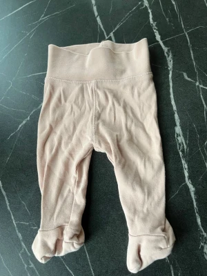 Ljusrosa babybyxor med fot - Säljer ett par ljusrosa babybyxor med fot i mjukt bomullstyg. Byxorna har bred mudd i midjan för extra komfort och är perfekta för små barn. Passar till dig som gillar enkla och stilrena plagg till de minsta.