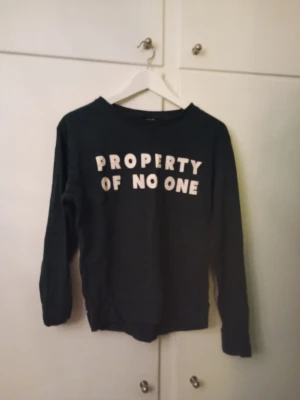 Grön sweatshirt med texttryck - Cool grön sweatshirt med vit text 'PROPERTY OF NO ONE' på bröstet. Tröjan har rund halsringning och långa ärmar. Perfekt för dig som gillar statement-plagg och en avslappnad stil.