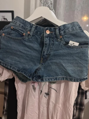Blå jeansshorts med fem fickor - Snygga blå jeansshorts i klassisk modell med fickor och kopparfärgade knappar. Shortsen har normal passform och bälteshällor i midjan. Perfekta för varma dagar och enkla att matcha med olika toppar.
