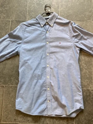 Ljusblå skjorta från Tommy Hilfiger - Klassisk ljusblå skjorta från Tommy Hilfiger med button-down krage och små logobroderi på bröstet. Skjortan har långa ärmar, vita knappar framtill och är tillverkad i mjuk bomull. Perfekt för en clean och stilren look. Ny pris runt 1000 kr 