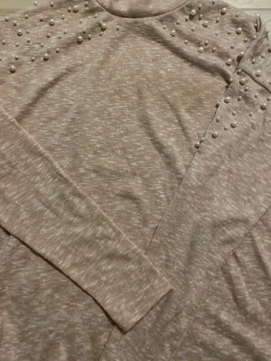 Hej! Säljer denna tröjan är jättefin använd 4 gånger säljer för jag inte har på mig den ofta den är i storlek S passar däremot till mindre storlekar  - Trendig beige stickad tröja med långa ärmar och dekorativa pärlor på axlarna. Tröjan har en mjuk, melerad struktur och rund halsringning. Perfekt för dig som vill ha en stilren men ändå unik look.