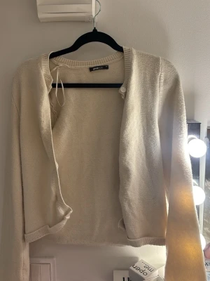 Beige kofta från Gina Tricot - Mysig beige kofta från Gina Tricot med långa ärmar och ribbade muddar. Koftan har en enkel design med knappar framtill och är perfekt att slänga på sig över en t-shirt. Mjuk och skön känsla, passar till många outfits.