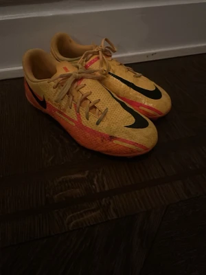 Nike Mercurial gula fotbollsskor - Säljer ett par Nike Mercurial fotbollsskor i gul färg med svarta och orange detaljer. Skorna har snörning och en låg profil som ger bra bollkontroll. Tillverkade i syntetmaterial för lätt vikt och smidig känsla på planen. Perfekta för dig som vill sticka ut på matchen!