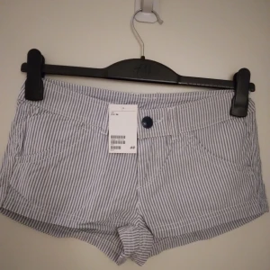 NYA, OANVÄNDA randiga shorts. Ljusblå / vit. Storlek: 34 / XS-SMALL. Felfria. - Helt NYA och oanvända fina vita/ljusblå smalrandiga shorts. Har 2 fickor fram och 2 fickor bak, samt hällor för skärp. Stängs med knapp och dragkedja framtill. Storlek: 34/XS-SMALL Material: Bomull. Felfria. Etiketter/tags sitter kvar. Nypris var 149 kr.