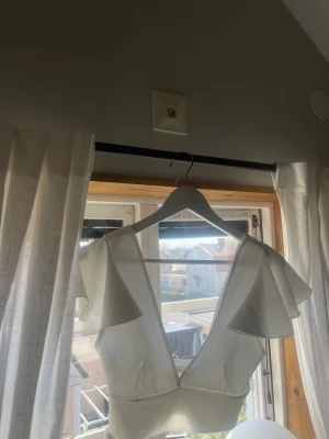 Vit topp🤍 - Säljer denna super fina vita sommar toppen🤍Den har volang liknande detaljer vid axlarna och är djup fram och baktill! Endast andvänd vid ett fåtal tillfällen och passar både XS och S!🤩