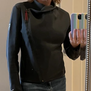 Puma Ferrari zip med snygga detaljer - Svart ziptröja med röda detaljer och Ferrari-logga på ärmen. Dragkedja på sidan fram ger snygg passform och fint fall i halsen. Fickor fram. Superskön! Som ny. 