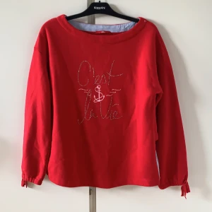 Unik tjocktröja  - Röd tjocktröja med ”C’est la víe” skriver i paljetter. Baksidan har en randig tygdel som är lite tunnare än resten. 