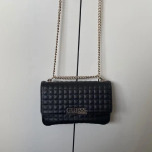 Guess Axelremsväska (ej förfalskning) - Använd ett fåtal gånger 3-4 år sedan, men i fint skick och har inga defekter. Har tappat kvittot men prislappen finns kvar. Dustbag medföljer.  Frakt 69 kr