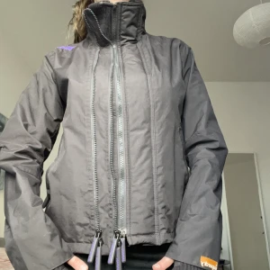 Vindjacka superdry - Mörkbrun/svart jacka storlek s, passar också xs. Snygga detaljer, tre dragkedjor lila text på Axel fram och bak. Nästan aldrig använd! 