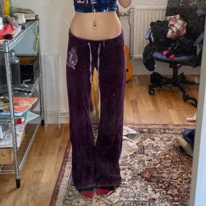 Lila gamla Juicy Couture byxor - Äkta lågmidjade Juicy Couture byxor i lila, ganska långa och lite slita längst ner (skriv för bild) köpta på plick för ett tag sedan helt okej använda, några rosa fläckar sen innan (skriv för bild) står M på lappen men skulle säga att dom passar som S