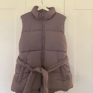 Väst  - Lila dunväst med snörning i midjan, använd en gång 