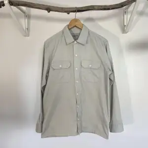 A used beige/grey Carhartt shirt in M - Small ink stain on the right pocket.