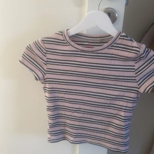 Rosa randig tröja - Jag säljer en rosa med lite ränder i färgen svart,grå och vit. Den är i storlek 134/140. Säljer pågrund av förlusten. Den är inte smutsig och har inga fläckar. Den tvättas innan det skickas. Den är köpt från H&M.