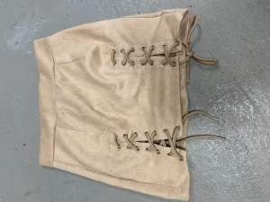 Kjol i mjukt material - Med detaljer av snörning i fram. Fint skick använd fåtal ggr. Beige färg 