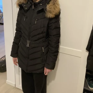 Hollies jacka - En jätte fin märkes jacka från HOLLIES, med äkta päls. Den är i bra skick. Den är i en fin svart färg och har ett bälte som kommer med. En vinter/höst jacka. Vid intresse så kan närmare och bättre bilder skickas